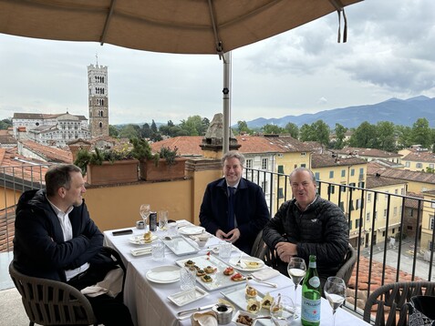 a group of men sitting at a table with food and drinks on a balcony